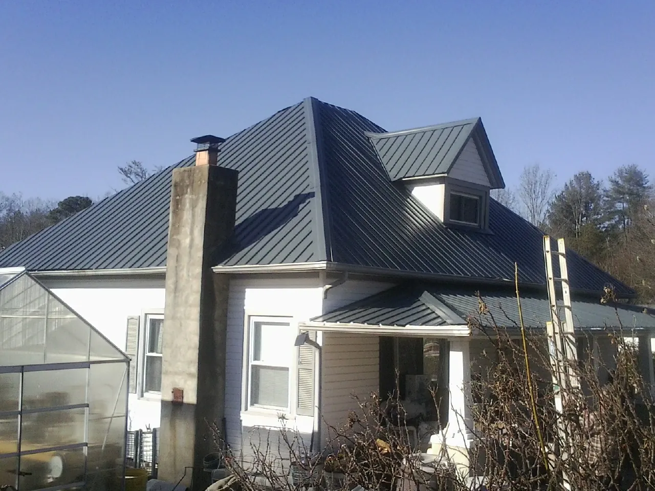 Dark blue standing seam metal roof on a white farmhouse with dormer — Slate & Tile Roof Repair by Roofing Brothers in Sedgwick