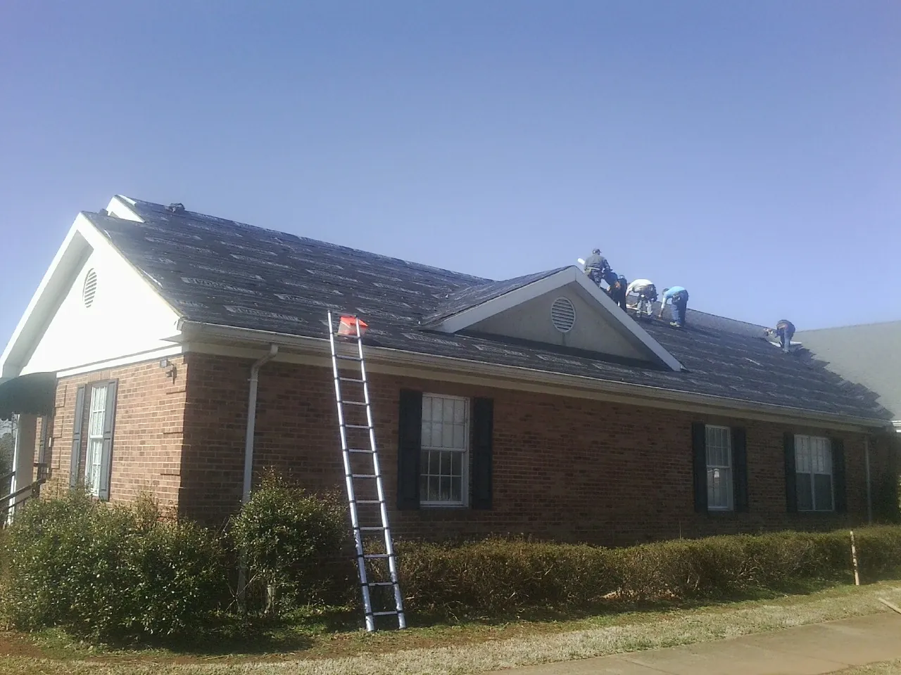 Crew tearing shingles off a brick ranch roof with a ladder set — Emergency Roof Repair work by our crew in Sedgwick