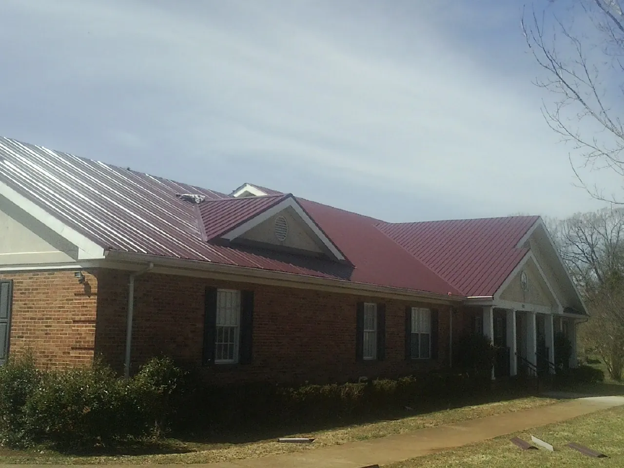 Red metal roof with gabled entries on a long brick building, from a Hail Damage Roof Repair job in Sedgwick