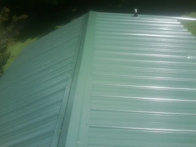 New green metal panels meeting at the ridge of a roof — Flat Roof Repair work by our crew in Sedgwick