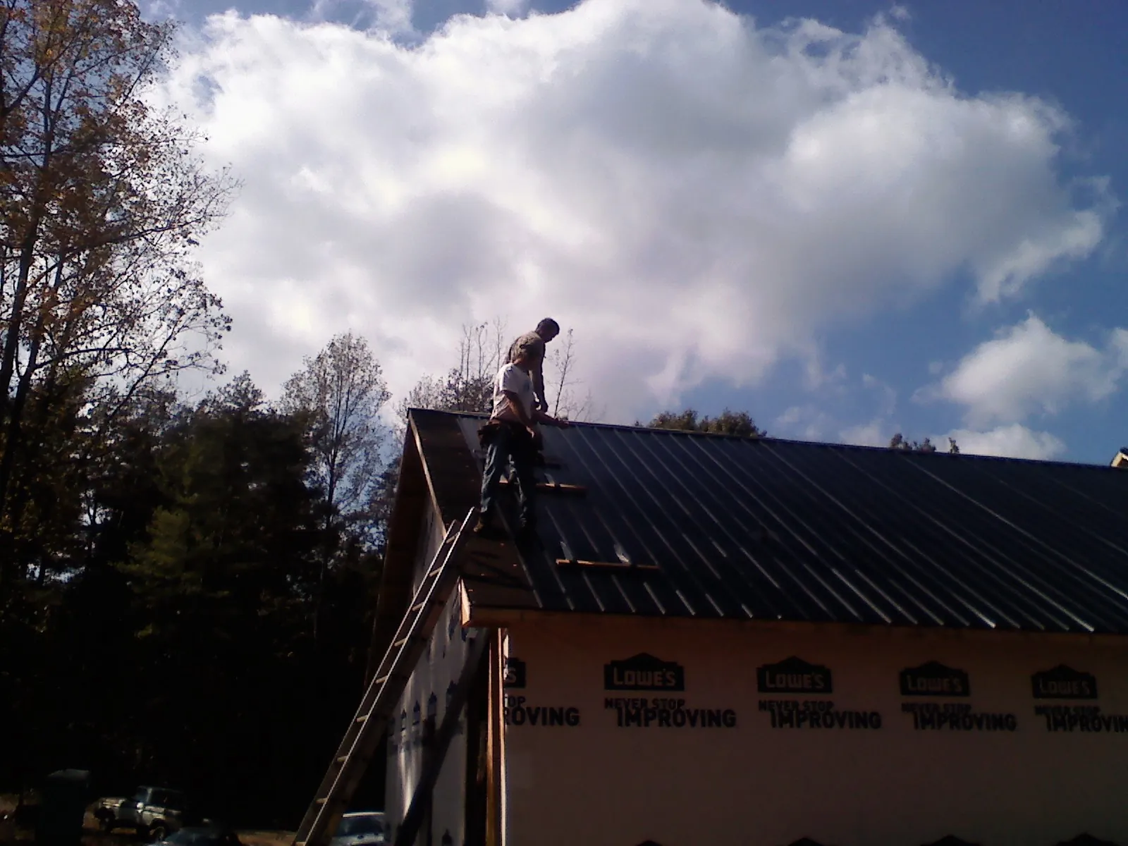 Roofer fastening dark metal panels high against a cloudy sky, from a Roof Inspection job in Sedgwick