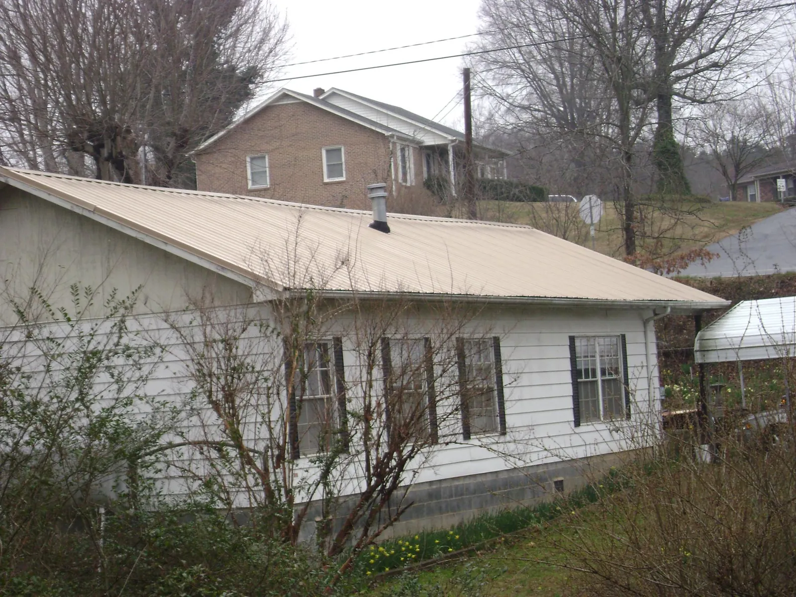 Tan metal roof on a white sided house set into a hillside — Commercial Roofing by Roofing Brothers in Sedgwick