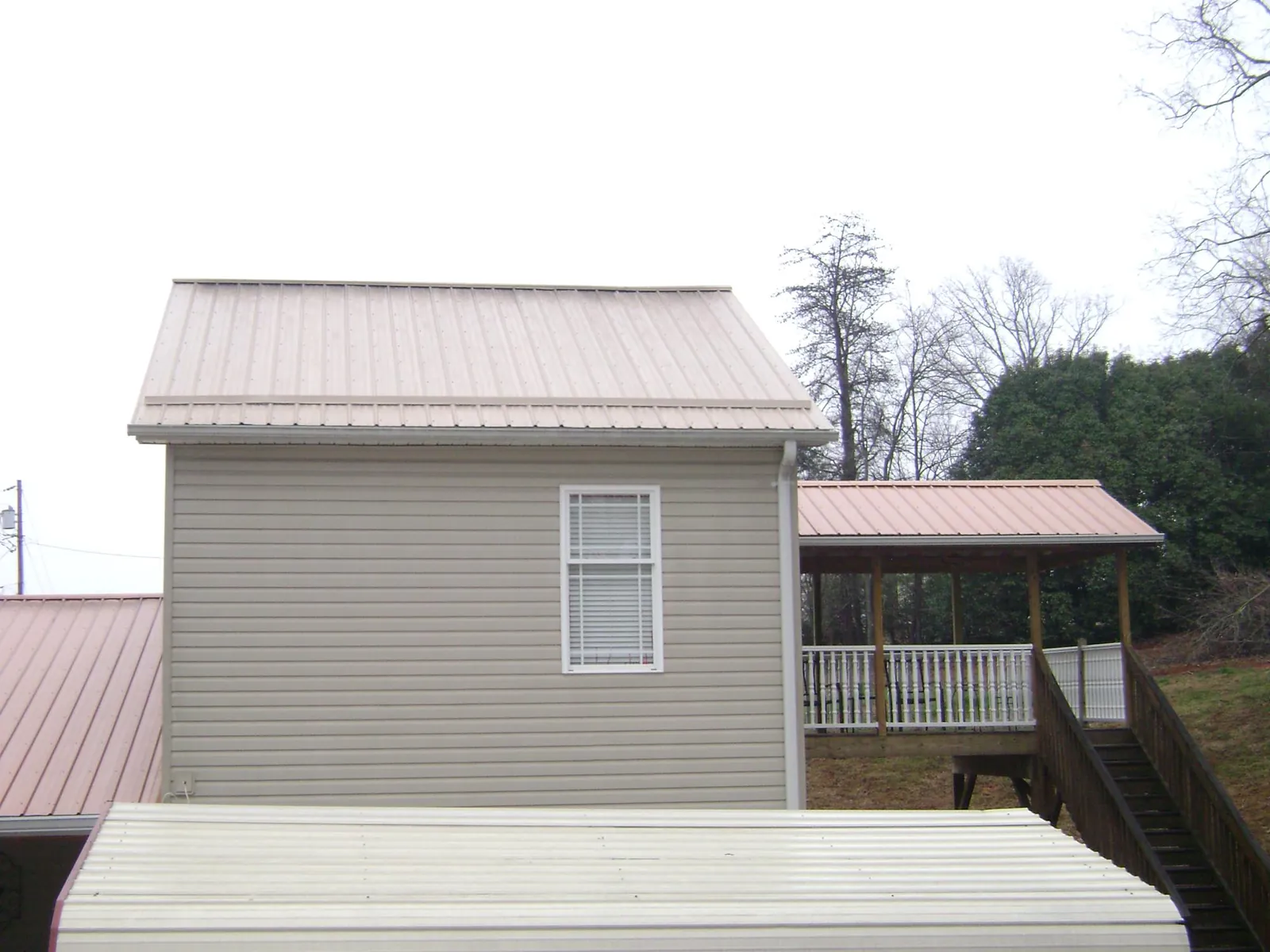 Tan metal roofs on a two story addition and attached porch, from a Roof Replacement job in Sedgwick